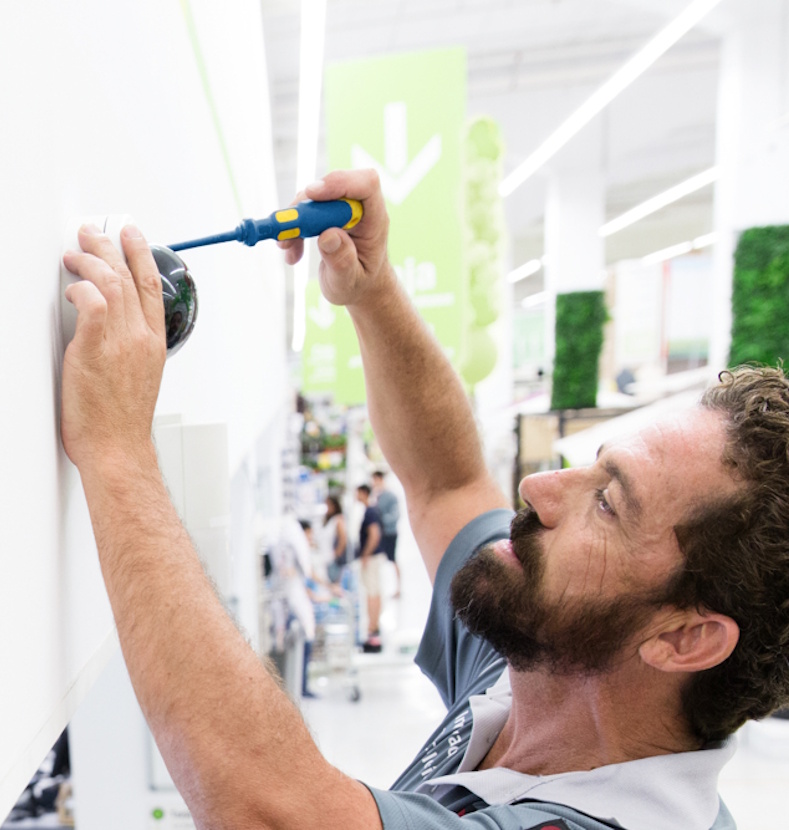 Un installateur visse une caméra de sécurité sur le mur d’un magasin